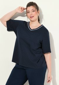 Námořnické modré tričko s krátkým rukávem a puntíky, V-výstřih s bílým lemem, spárované s jednobarevnými námořnickými kalhotami. Hladká textura látky.