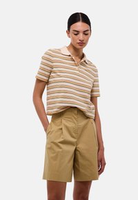 Polo rayé en crème, orange et marron avec des manches courtes et un col ; associé à un short beige taille haute plissé.