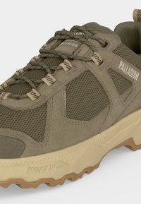 Κοντινή λήψη ενός πεζοπορικού παπουτσιού Palladium Gore-Tex σε ελιά απόχρωση με διχτυωτά πάνελ, μπεζ ανθεκτική σόλα και στρογγυλά κορδόνια με σχέδια.