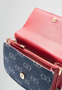 Džínsová kabelka s červeným koženým interiérem, obsahující zipovou kapsu a zlaté kovové doplňky. Monogramový vzor na modrém exteriéru.
