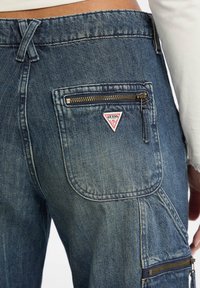Dunkelblaue Denim-Jeans mit einem verblassten Erscheinungsbild. Verfügt über eine Reißverschlusstasche, ein dreieckiges Logo-Patch und verstärkte Nähdetails.