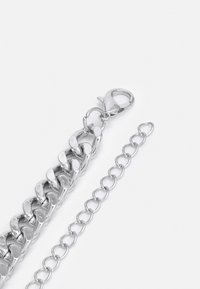 Bracelet en métal argenté présentant des maillons en curb et un fermoir en forme de homard, avec une chaîne d'extension supplémentaire et des maillons ovales. Texture lisse.