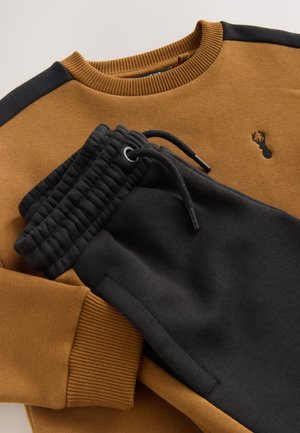 Brun sweatshirt med svarta axelaccents och liten broderad logotyp, kombinerad med svarta joggers med dragsko i midjan och ribbade muddar.