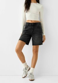 Shorts de mezclilla negra con dobladillo deshilachado, combinados con una camiseta corta de manga larga blanca y zapatillas plateadas brillantes con calcetines color crema.
