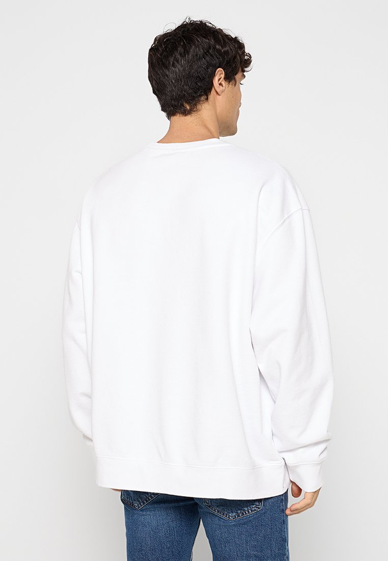 Sudadera de algodón blanca con un corte relajado, hombros caídos y puños acanalados. Diseño simple sin patrones ni acentos visibles.