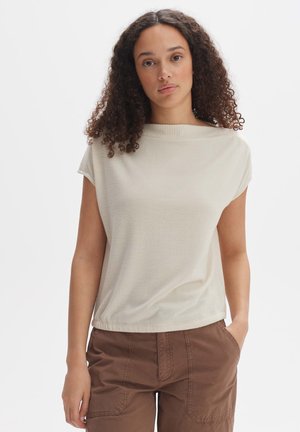 Hellbeige Kurzarmoberteil mit geripptem Rundhalsausschnitt und lockerer Passform, kombiniert mit braunen Cargo-Hosen. Glatte Textur.