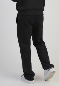 Crne trenirke opuštenog kroja, s elastičnom gumom u struku i na manžetama. Uparene s bijelim tenisicama koje imaju teksturiranu potplatu.