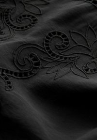 Zwart stof met ingewikkelde zwarte borduursels en zwierige en florale patronen. Gladde textuur met gedetailleerde stiksels zichtbaar.