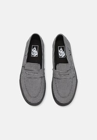 Paire de chaussures Vans slip-on en motif pied-de-poule noir et blanc avec semelles noires, vue de dessus sur un fond blanc.