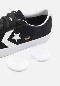 Schwarze Wildleder-Sneaker mit weißen Akzenten und einem Stern-Logo, versehen mit goldenen "CONS"-Buchstaben. Enthält zwei Paar weiße Schnürsenkel.
