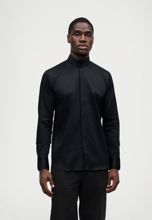 Musta pitkähihainen paita, joka on valmistettu sileästä kankaasta ja jossa on korkea kaulus sekä tiukka muotoilu. Hihansuut ovat myös mustat ja niissä on hieman kiiltoa.