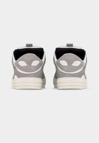 Ζευγάρι γκρι σουέντ αθλητικά παπούτσια, εμφανιζόμενα από πίσω, με λευκές σόλες και μπαλώματα σε σχήμα εξωγήινου στα τακούνια.
