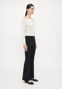 Off-the-shoulder witte top gecombineerd met zwarte flared broek, beide in een slim fit stijl; de top heeft een geribbelde halslijn en een gladde textuur.