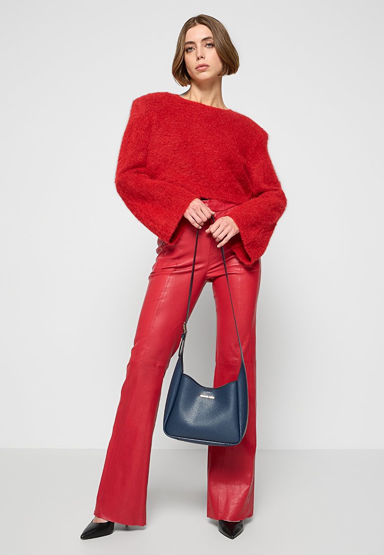 Pull rouge en peluche avec des manches larges, associé à un pantalon en cuir rouge ajusté. Le modèle tient un sac à main bleu marine, portant des escarpins noirs à bouts pointus.