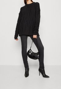 Suéter negro de punto con patrón texturizado, combinado con jeans skinny oscuros y botas de tacón puntiagudas negras. Lleva un pequeño bolso negro.