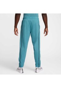 Teal joggebukser med slim fit, elastisk liv, sidelommer og svarte side-striper. Glidelåser ved ankler for justerbar passform.