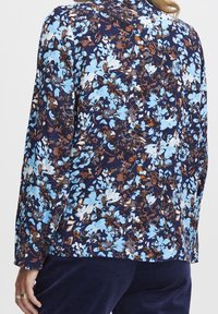 Blusa floreale blu navy con un motivo di fiori blu chiaro, bianchi e marroni, maniche lunghe e vestibilità rilassata. Tessuto morbido e leggero.