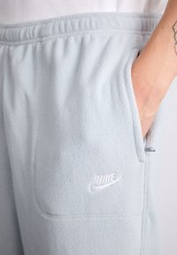 Svijetloplave flis trenirke s elastičnom strukom, bočnim džepovima i bijelim izvezenim Nike logotipom na lijevoj nozi. Mekan dodir.