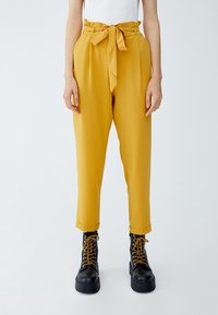 Senapsgula högmidjade byxor med framplytt, knytbälte och svarta snörstövlar med chunky sula.