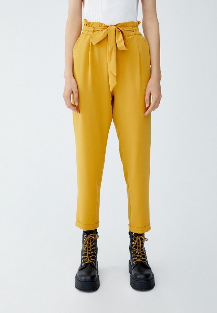 Senapsgula högmidjade byxor med framplytt, knytbälte och svarta snörstövlar med chunky sula.
