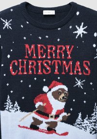 Maglione in maglia blu navy con un orso in tuta rossa da Babbo Natale che scia, con la scritta "BUON NATALE" in lettere rosse in grassetto e fiocchi di neve bianchi sparsi su tutta la maglia.