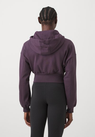 Cropped purple hoodie made of soft fabric, featuring a hood and loose sleeves. Worn with black leggings, showcasing a relaxed fit.