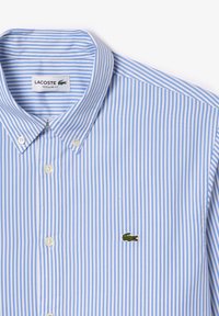Camisa de botones a rayas en azul claro y blanco, hecha de algodón, con un pequeño logo de cocodrilo verde en el pecho, corte regular.