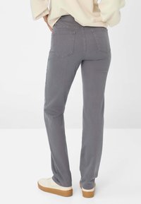 Graue Jeans mit geradem Bein, ausgestattet mit zwei Gesäßtaschen und einem mittelhohen Bund. Kombiniert mit hellen Turnschuhen.