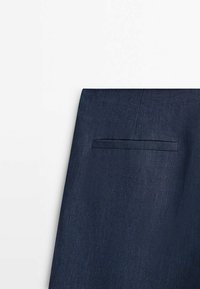 Gros plan d'un tissu bleu marine avec un détail de poche passepoilée horizontale sur un vêtement, probablement une partie d'un costume ou d'un blazer.