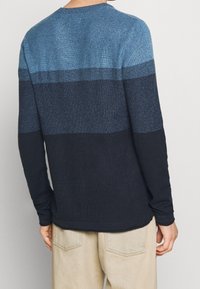 Långärmad tröja med en gradientdesign i nyanser av blått som övergår till mörk marinblå, texturerat stickat material och rund halsringning.