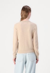Beżowy sweter z dzianiny, z długimi rękawami i okrągłym dekoltem, z prążkowanym dołem i mankietami, wykonany z miękkiego, fakturowanego materiału.
