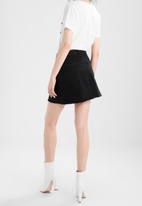 Mini falda de mezclilla negra con dobladillo deshilachado, cintura ajustada y dos bolsillos traseros, combinada con una camiseta blanca y botines blancos de tacón alto.