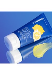 Tubo azul exprimible de "Exfoliante Suave de Limón" con etiqueta amarilla, gráfico de limón, tapa blanca y una pequeña cantidad de exfoliante en gel al lado.