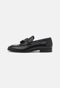 Mocasines de cuero negro con textura de cocodrilo, tacón plano, borlas decorativas y un acento de hebilla en tono dorado. Vista lateral.