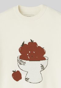 Pull en crème avec un design tricoté représentant un bol de pommes rouges et une petite pomme sur le côté, agrémenté de feuilles vertes.