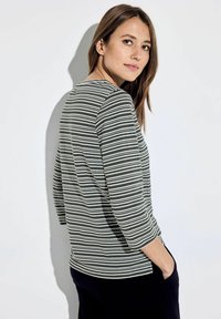 Gestreepte lange mouwen top in groen en wit, met een ronde hals en een ontspannen pasvorm met een zijsplit, weergegeven op een lichte achtergrond.