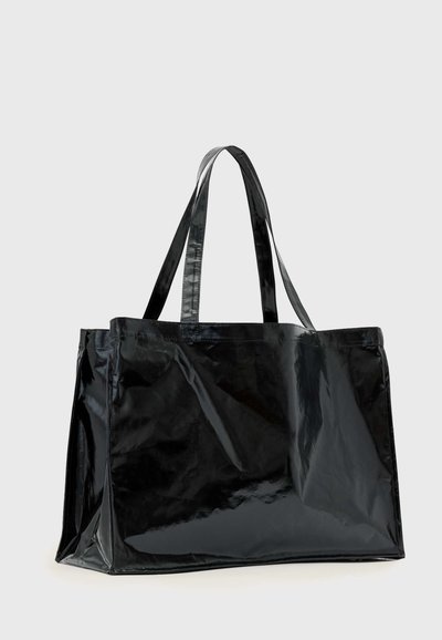 Sac cabas noir brillant avec deux poignées, forme rectangulaire et surface lisse légèrement froissée sur un fond clair uni.