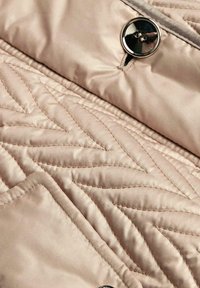 Gestepptes beige Stoff mit glatter Textur, das ein dekoratives Zickzackmuster und ein glänzendes schwarzes Knopfdetail aufweist.