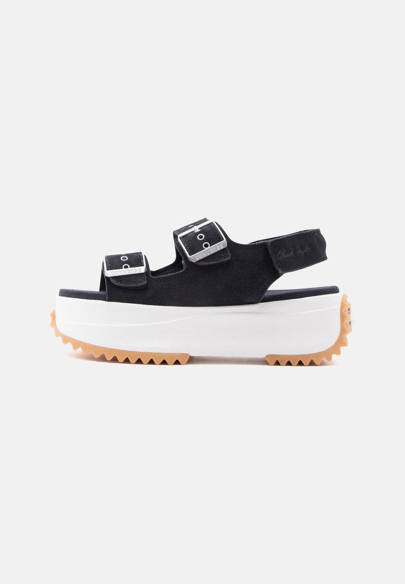 Schwarze Plateau-Sandale mit zwei verstellbaren Riemen mit Schnallen, einem Rückriemen, dicker weißer Sohle und braunem, gezacktem Profilboden.