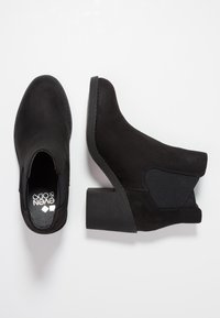 Bottines noires en daim, avec un talon épais, un panneau latéral élastique et un bout arrondi. La semelle a un design texturé pour une meilleure adhérence.