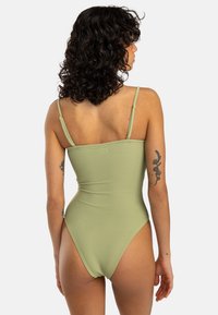 Maillot de bain une pièce vert à côtes avec de fines bretelles réglables, des découpes hautes et un dos sans coutures. Détail de marquage minimal au dos.