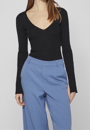 Haut noir à manches longues côtelé avec un décolleté en V profond, associé à un pantalon taille haute bleu clair à coupe ajustée et poches latérales.