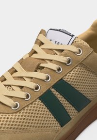 Baskets en mesh marron clair et daim avec des lacets beige, des bandes latérales vert foncé et un logo Steve Madden visible sur la languette.