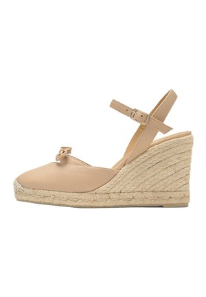 Alpargata beige con cuña, suela de yute trenzado, tira en el tobillo con hebilla, puntera cerrada y pequeño lazo decorativo en la parte superior.