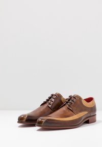 Chaussures habillées en cuir marron avec un design bicolore, une finition lisse, un bout arrondi et des accents tan contrastants ; doublure rouge.