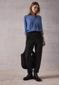 Lyseblå denim skjorte med knapper, sorte bukser med elastik og snøre, samt sorte ankelstøvler med kraftige såler. Enkel design uden mønstre.