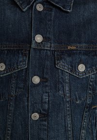 Tmavě modrá džínová bunda s kovovými knoflíky s vyraženým nápisem "Ralph Lauren Polo" a náprsními kapsami s klopami a oranžovým prošíváním.