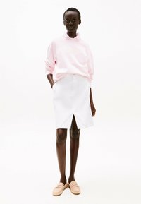 Felpa rosa con collo alto, gonna bianca a lunghezza ginocchio con spacco frontale e scarpe beige chiare slip-on. Texture lisce.