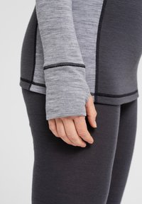 Grå langærmet top med en tætsiddende design, der har tommelfingerhul og mørke sømme, tilpasset med mørkegrå leggings i et tekstureret materiale.