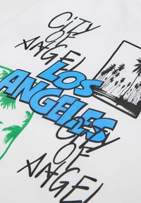 Bílá bavlněná tričko se grafikou: "LOS ANGELES" v tučném modrém písmu, tropické siluety palem v zelené a ručně psaný text v černé.